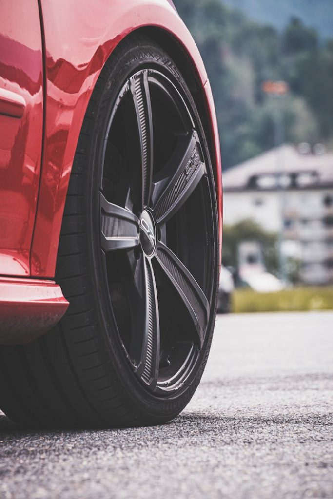 Close-up view of a red cars wheel with black rim on a sunny day outdoors.